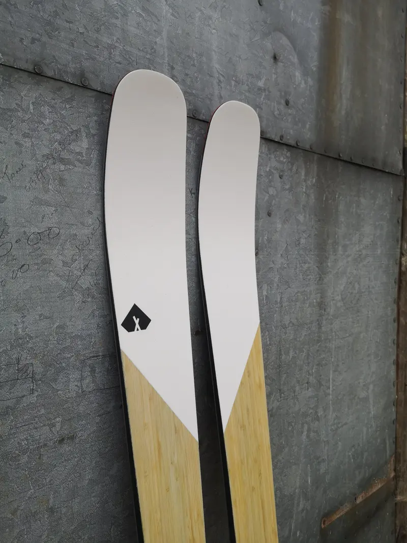 Pair of white and bamboo skis leaning against a concrete wall