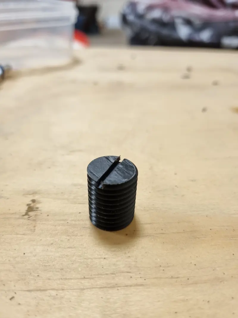 Small black CNC-milled threaded part with a slotted head on a workbench